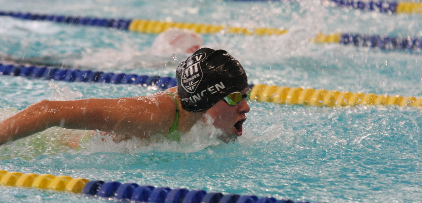 Schwimmerin im Wettkampf, die im Schmetterlingsstil auf einer Bahn schwimmt, mit Spritzwasser und bunter Markierung.