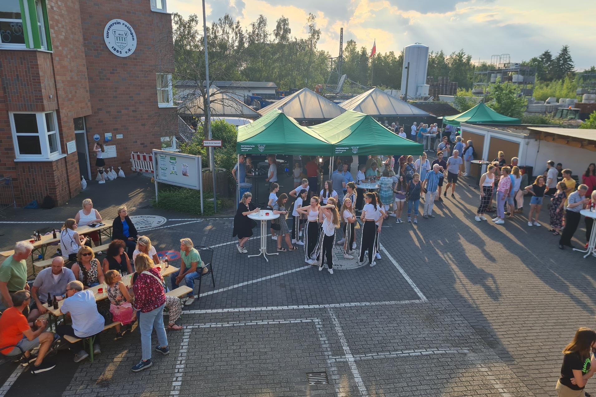 Menschen versammeln sich auf einem Platz vor einem Gebäude, umgeben von Zelten und Ständen bei einer Veranstaltung.