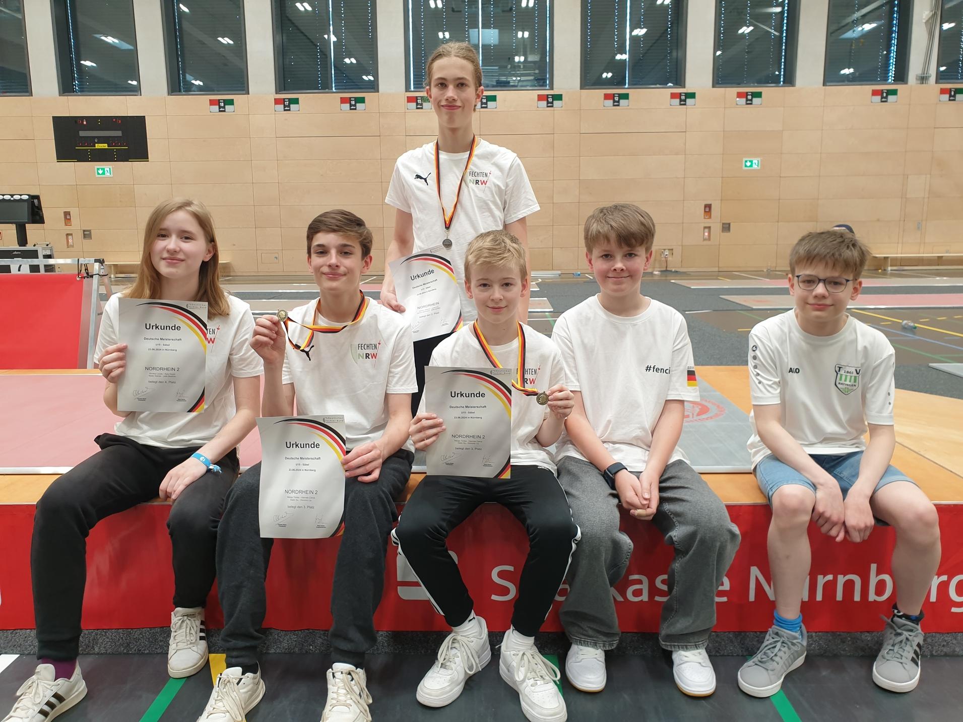Sechs Jugendliche sitzen auf einer Bank, halten Urkunden und Medaille in einer Sporthalle.