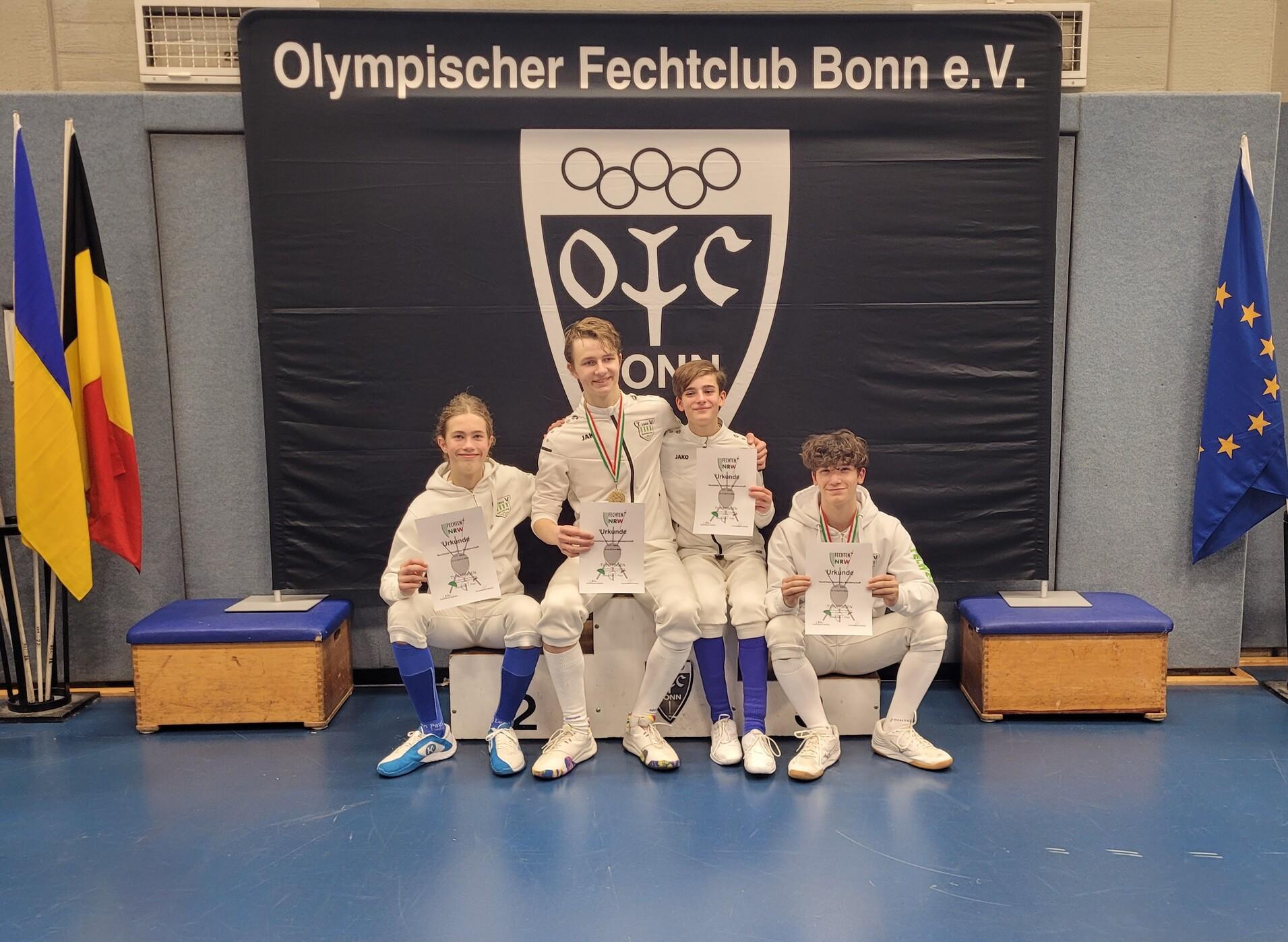Vier Fechter in Trainingsanzügen halten Urkunden und stehen vor einem Banner des Olympischen Fechtclubs Bonn e.V.