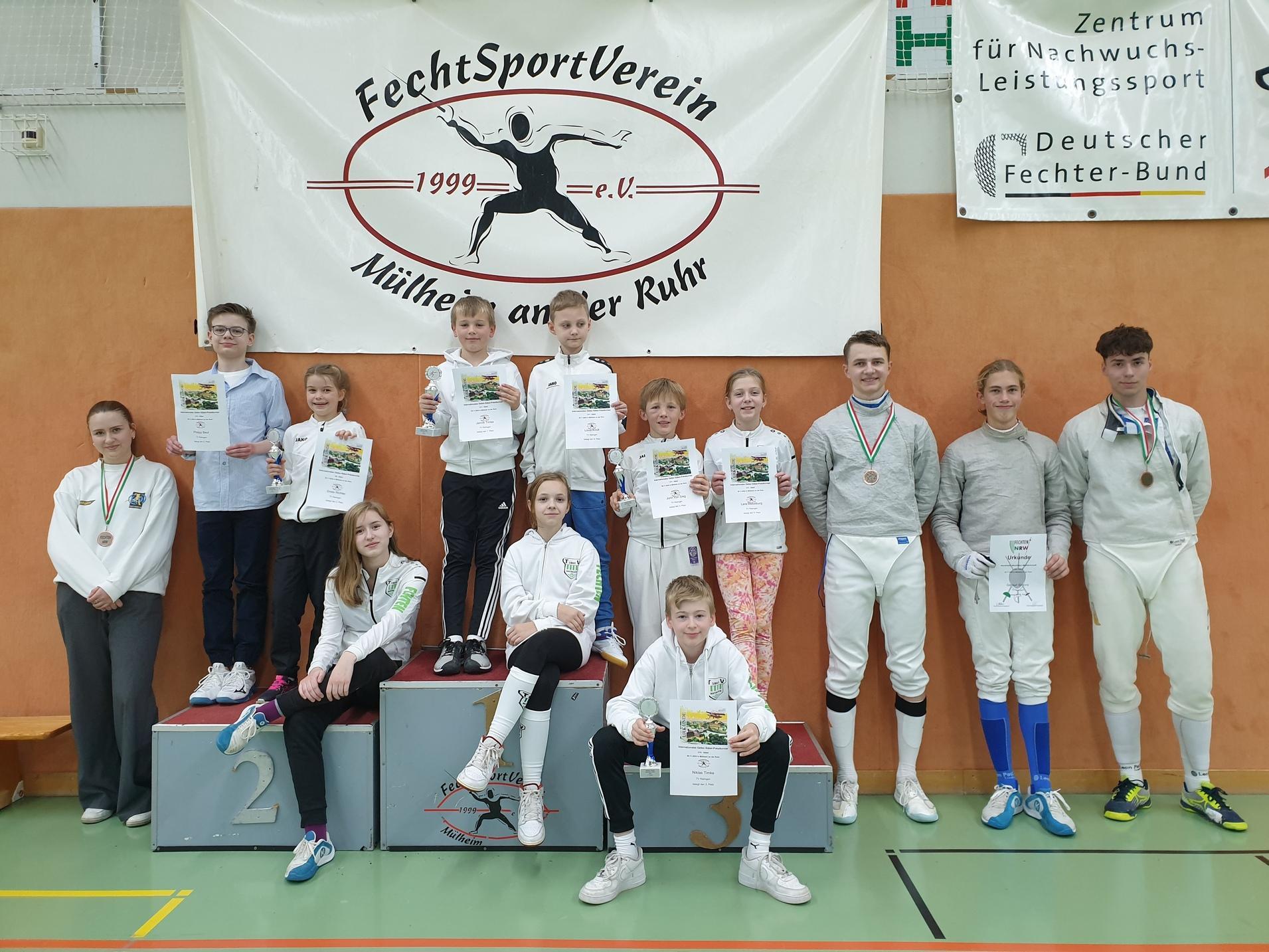 Gruppensfoto von Fechtteilnehmern mit Urkunden und Medaillen vor einem Vereinsbanner. Präsentation der Sieger.