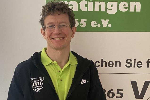 L&auml;chelnder Mann in Sportbekleidung steht vor einem Banner des Turnvereins Ratingen 1865 e.V. mit gr&uuml;ner Schrift.