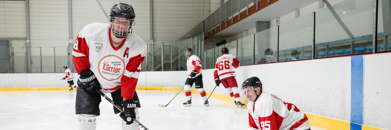 Eishockeyspieler in rot-weißen Trikots üben auf einer Eisfläche, während einer sich auf dem Eis abstützt.