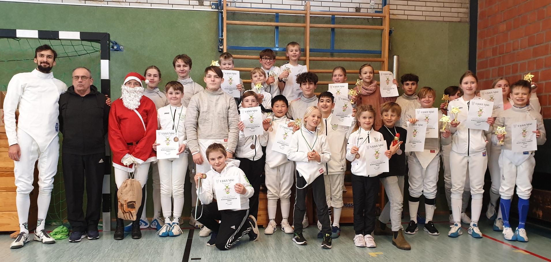 Gruppe von 20 Personen im Dojo, mit Fechtausrüstung, Medaillen und Urkunden, daneben ein Weihnachtsmann.
