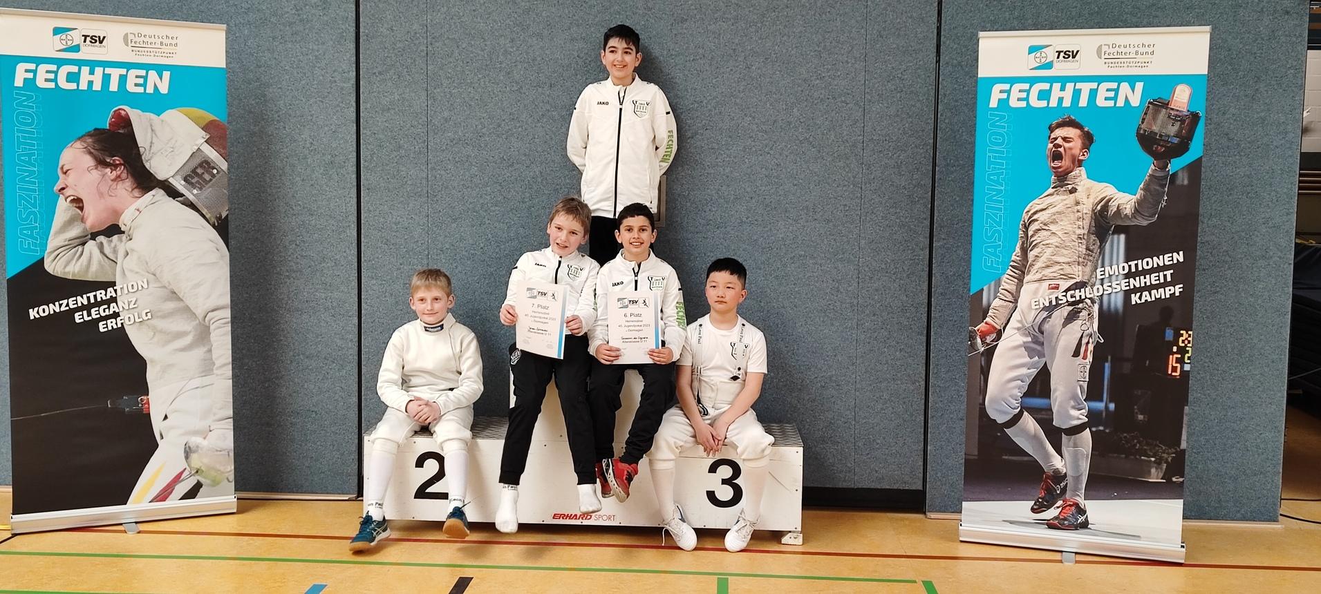 Fünf junge Fechter mit Urkunden sitzen und stehen auf einem Podest vor Bannern zum Thema Fechten.