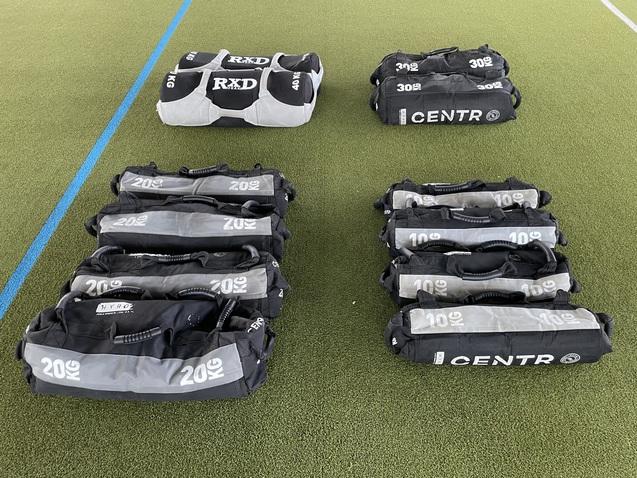 Trainingstasche mit verschiedenen Gewichten auf einem grünen Sportboden, darunter 10 kg und 20 kg Varianten.
