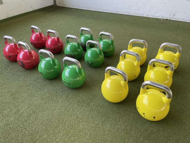 Reihe von Kettlebells in Rot, Grün und Gelb auf einem grünen Untergrund.