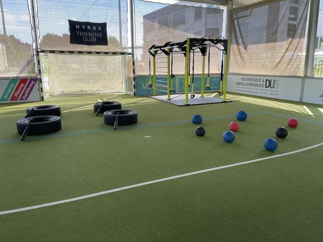 Trainingsbereich mit Reifen, einer Trainingsstation und bunten Bällen auf einem Kunstrasenboden.