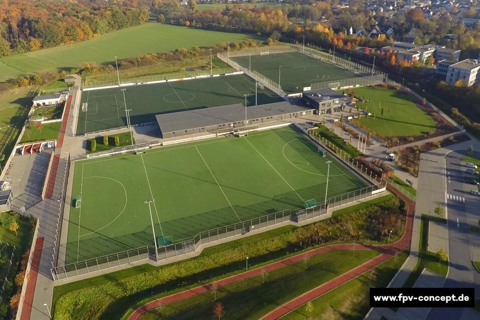 Luftaufnahme eines modernen Sportgel&auml;ndes mit zwei Fu&szlig;ballfeldern, einem Geb&auml;ude und umgebendem Gr&uuml;n.