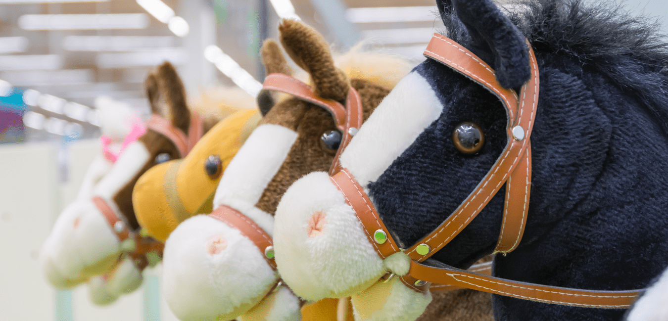 Reihe aus vier Stoffpferden in verschiedenen Farben mit Sattel und Zügel auf einem hellen Hintergrund.