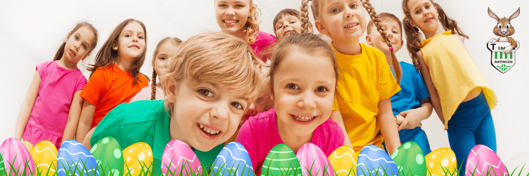 Gruppe von l&auml;chelnden Kindern in bunten T-Shirts vor Ostereiern in einer hellen Umgebung.
