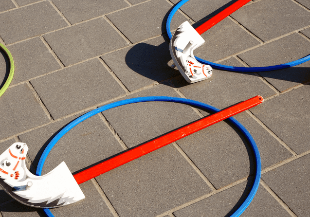 Zwei farbige Hula-Hoops und Spielgeräte mit roten Stangen auf grauen Pflastersteinen.