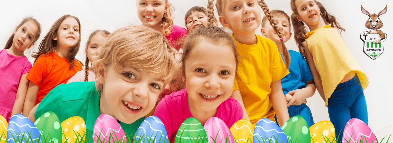 Gruppe von l&auml;chelnden Kindern in bunten T-Shirts vor Ostereiern in einer hellen Umgebung.