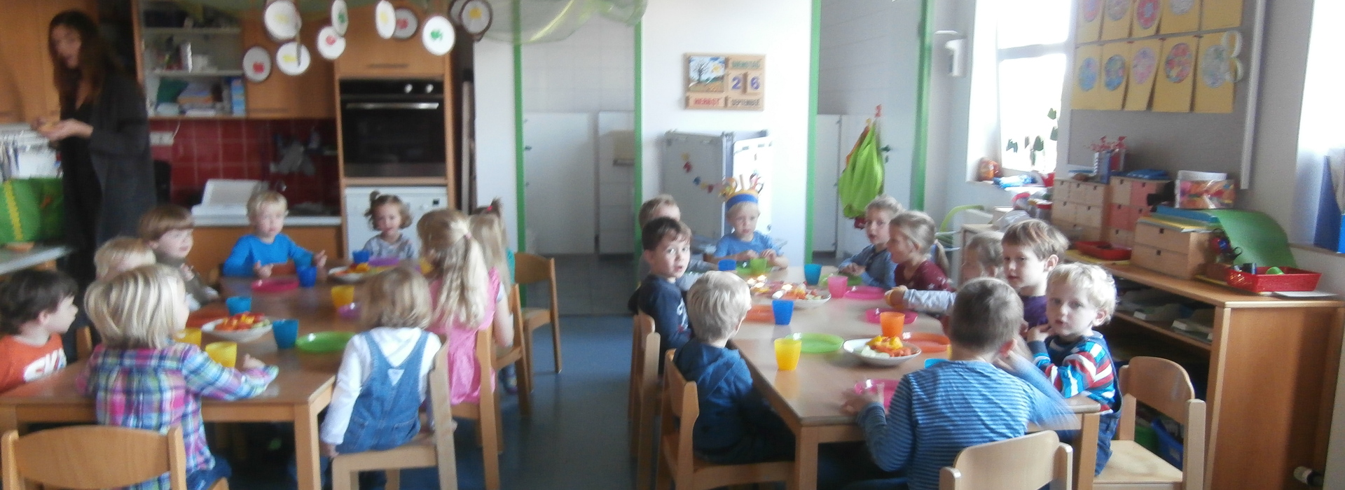 Gruppe von Kindern sitzt an einem Tisch mit bunten Tellern und Getr&auml;nken in einem hellen, dekorierten Raum.