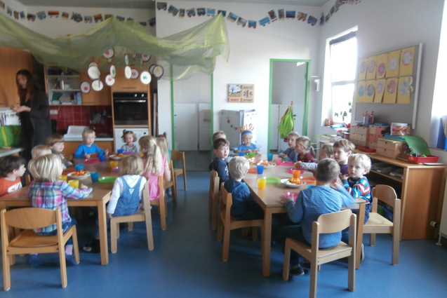 Gruppe von Kindern sitzt an einem Tisch mit bunten Tellern und Getr&auml;nken in einem hellen, dekorierten Raum.