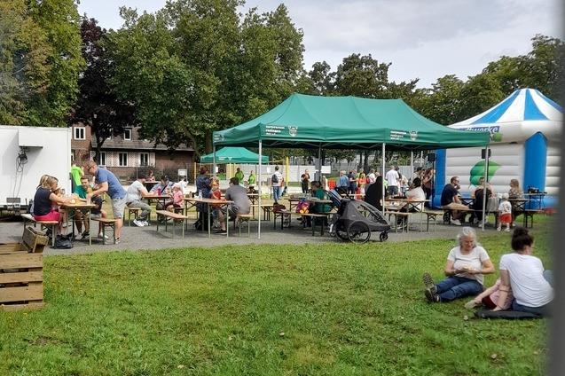 Veranstaltung im Freien mit gr&uuml;nen Zelten, Tischen und vielen Menschen, die sich unterhalten und speisen.