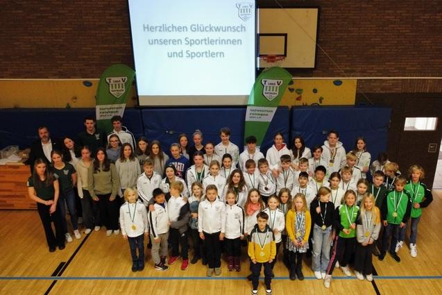 Gruppenfoto von Sportlerinnen und Sportlern mit Medaillen bei einer Ehrungsveranstaltung in einer Sporthalle.