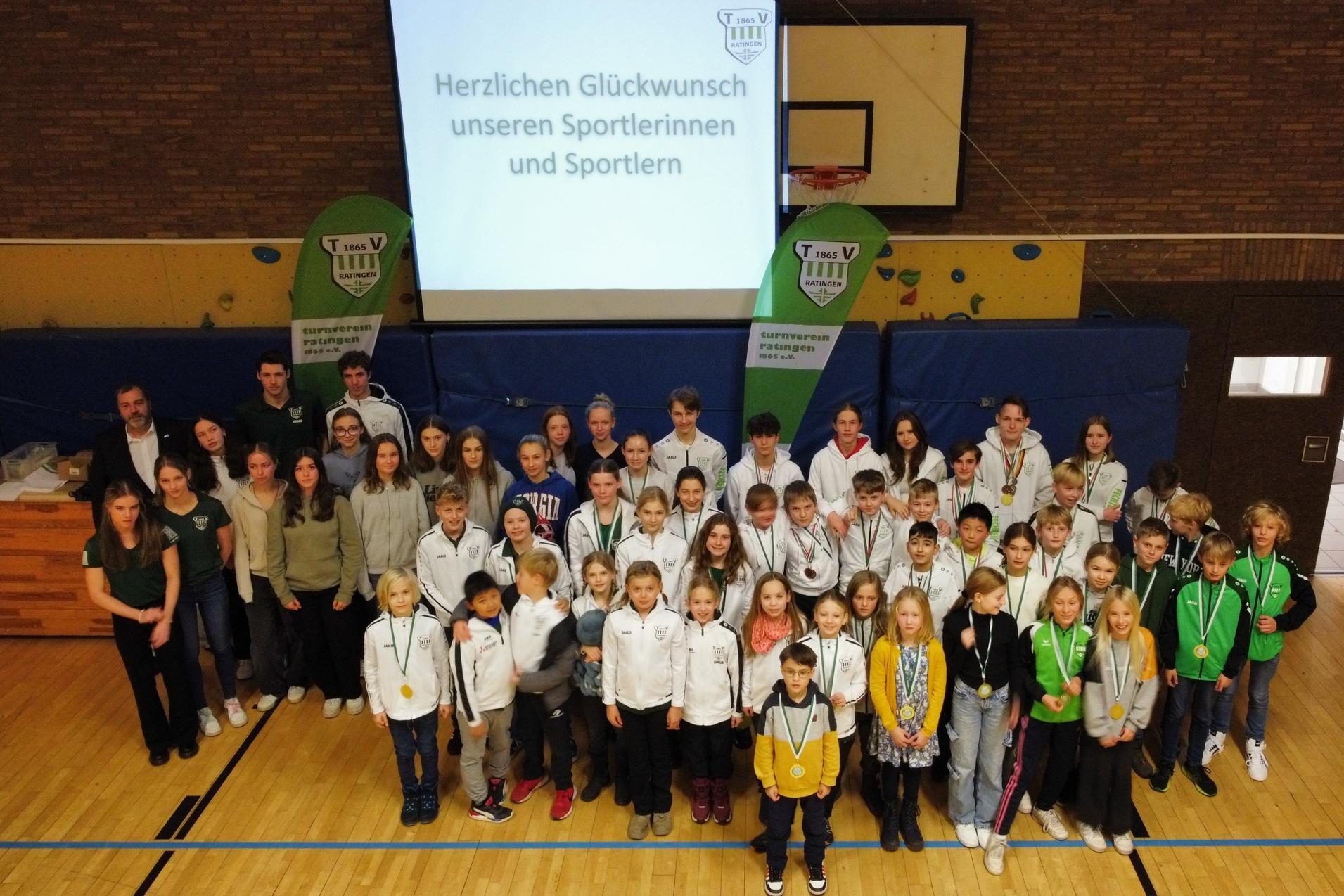 Gruppenfoto von Sportlerinnen und Sportlern mit Medaillen bei einer Ehrungsveranstaltung in einer Sporthalle.