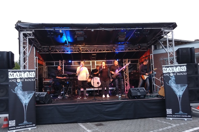 Live-Band auf der B&uuml;hne mit Gesang, Keyboard, E-Gitarre und Bannern im Hintergrund. Event in st&auml;dtischer Umgebung.