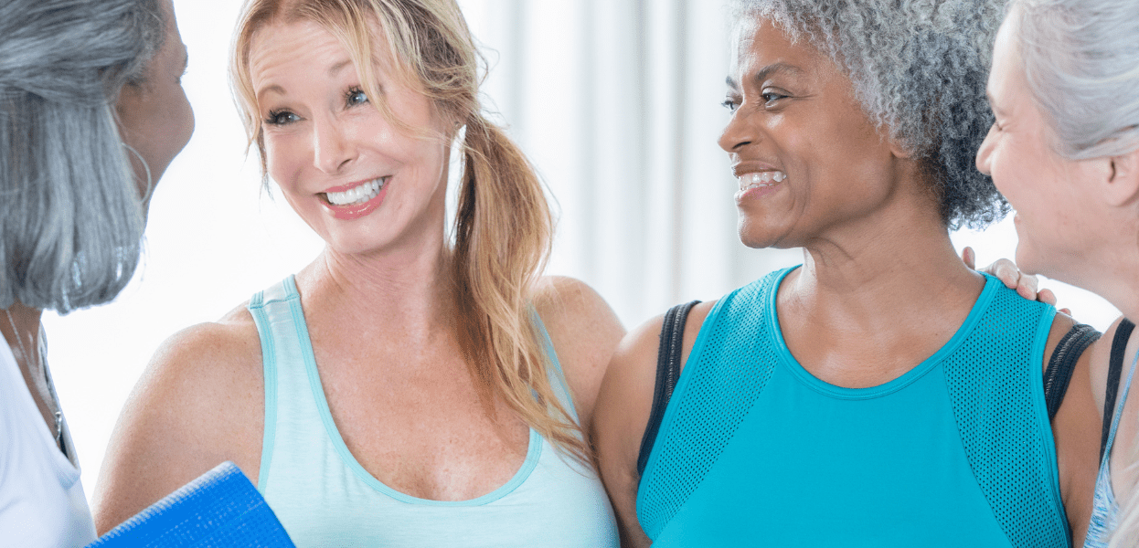 Vier Frauen lachen und unterhalten sich, w&auml;hrend sie Sportbekleidung tragen und eine entspannte Atmosph&auml;re genie&szlig;en.