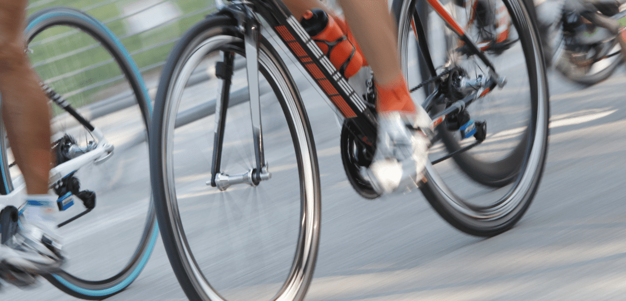 Drei Radfahrer in schneller Fahrt, Beine und Räder verschwommen dargestellt, auf einer Asphaltstraße.