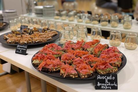 Teller mit belegten Broten, darunter Avocado und R&auml;ucherlachs, sowie Gl&auml;ser mit Creme auf einem Tisch.