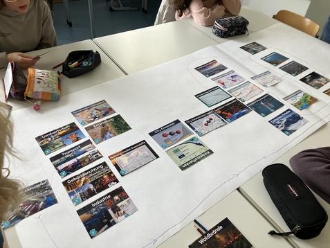 Tisch mit mehreren thematischen Karten zu Umwelt, Landwirtschaft, Transport und Industrie; persönliche Gegenstände im Hintergrund.