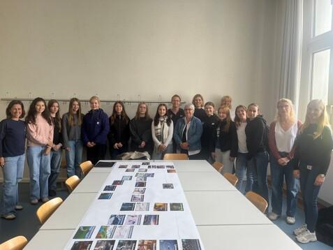 Gruppenfoto mit elf Frauen und Mädchen vor einem Tisch, auf dem Bilder ausgelegt sind, in einem hellen Raum.