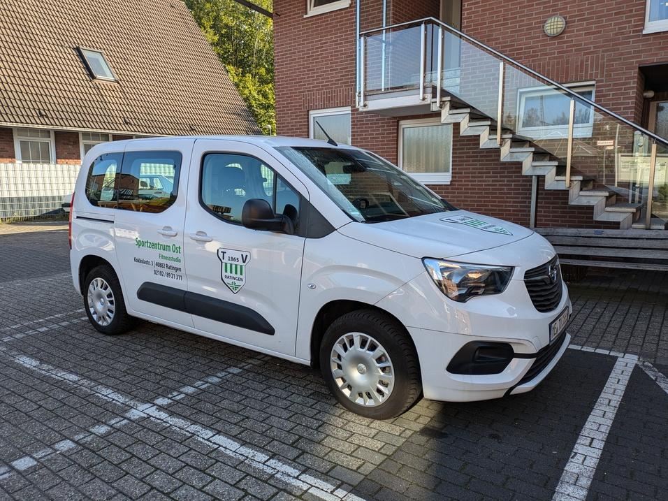 Weißer Transporter des Sportzentrums Ost auf einem Parkplatz vor einem Gebäude mit Treppe.