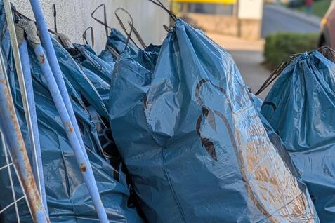 Blaue M&uuml;lls&auml;cke stehen neben einem Gehweg, w&auml;hrend ein Auto und ein Geb&auml;ude im Hintergrund sichtbar sind.