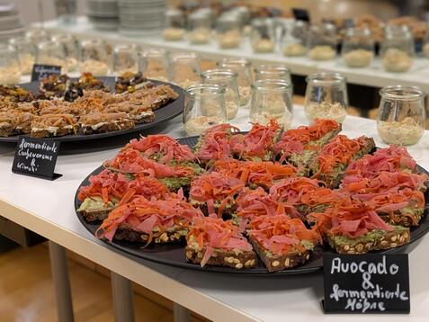 Teller mit belegten Broten, darunter Avocado und R&auml;ucherlachs, sowie Gl&auml;ser mit Creme auf einem Tisch.