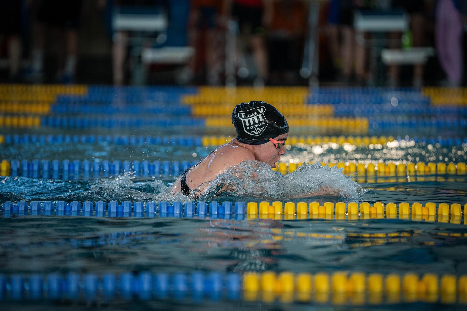 Schwimmerin in schwarzer Mütze gleitet durch Wasserbahnen mit gelben und blauen Markierungen in einem Wettkampfpool.