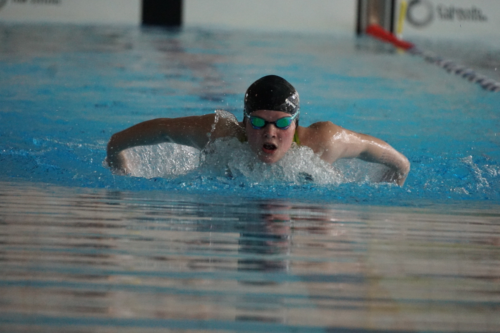 Schwimmer in Aktion beim Brustschwimmen, mit Schwimmbrille und Kappen, im Becken mit klarem Wasser.
