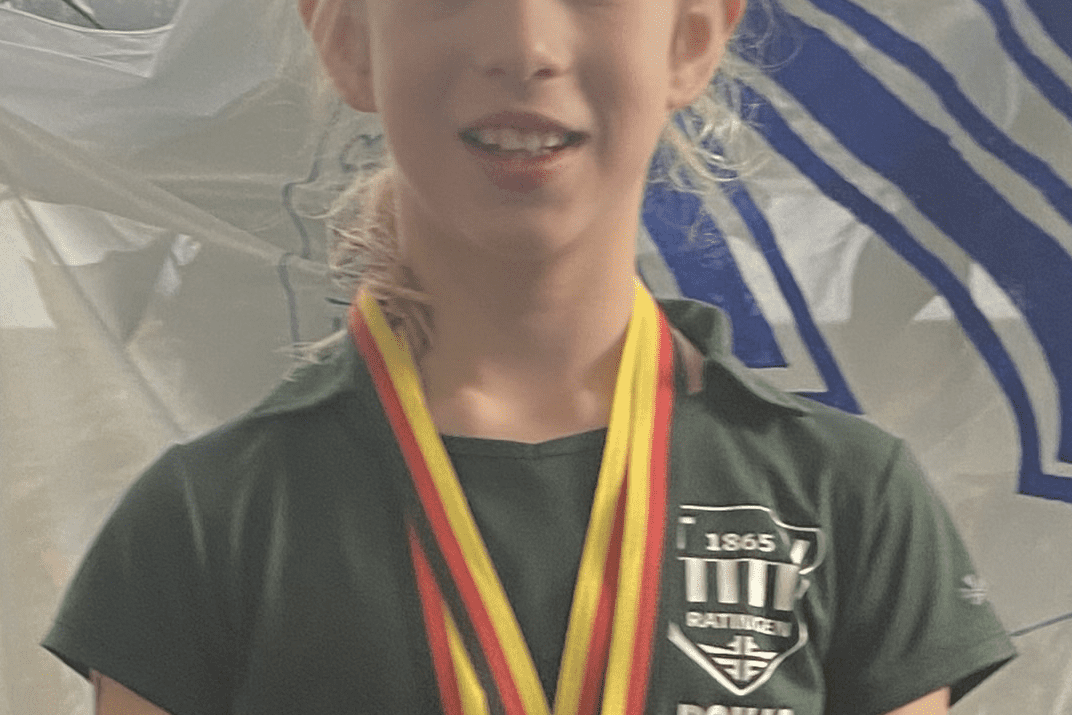 Portr&auml;t eines jungen M&auml;dchens in gr&uuml;ner Sportkleidung mit Medaillen um den Hals vor einem hellen Hintergrund.