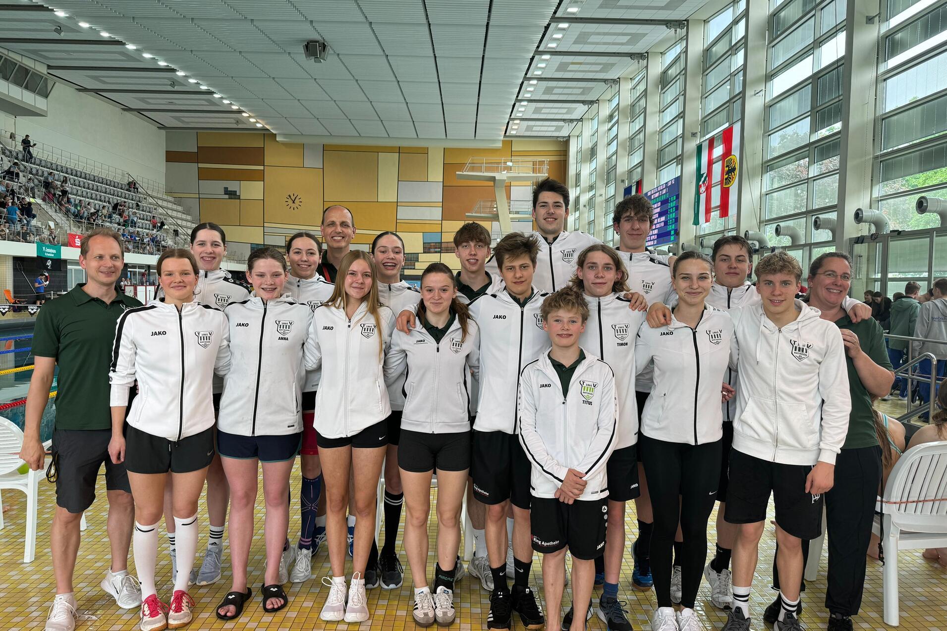 Gruppenzusammensetzung von Schwimmern in weißen Trainingsjacken, auf einer Schwimmveranstaltung in einer Halle.