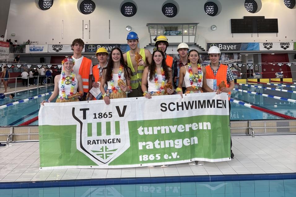 Gruppe junger Schwimmer in bunter Kleidung h&auml;lt ein Banner des Turnvereins Ratingen am Schwimmbecken.