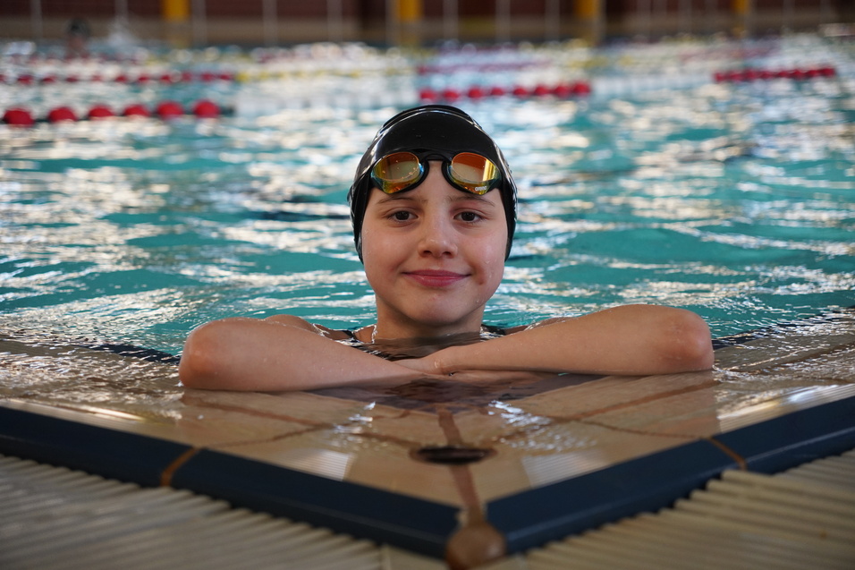Ein Junge mit Schwimmbrille und Badekappe lehnt am Beckenrand eines Schwimmbeckens.
