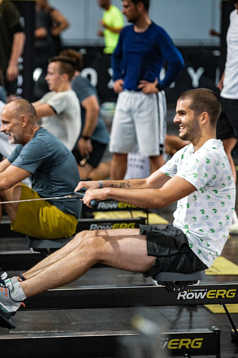 Gruppe von Sportlern, die auf Ruderger&auml;ten in einem Fitnessstudio trainieren, mit Fokus auf Technik und Motivation.