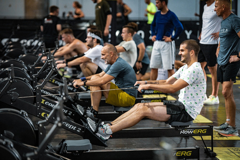 Gruppe von Sportlern, die auf Ruderger&auml;ten in einem Fitnessstudio trainieren, mit Fokus auf Technik und Motivation.