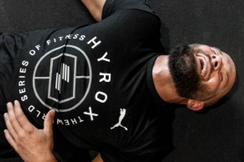 Mann liegt auf dem Boden in Sportkleidung, lächelt und schaut zur Decke, umgeben von einer schwarzen Unterlage.