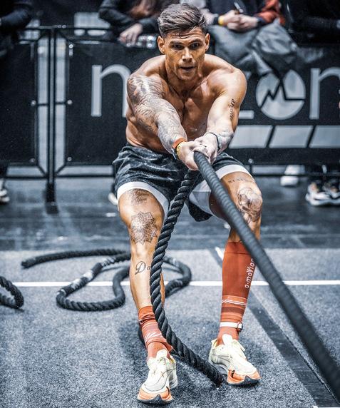 Ein muskulöser Mann zieht mit beiden Händen an einem dicken Seil während eines Wettkampfs. Zuschauer im Hintergrund.
