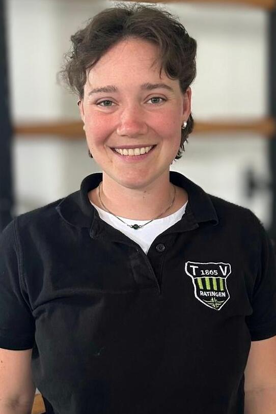 L&auml;chelnde Person mit kurzen Haaren, in schwarzer Polo-Uniform mit Logo, vor hellen Hintergrund.