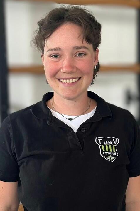 L&auml;chelnde Person mit kurzen Haaren, in schwarzer Polo-Uniform mit Logo, vor hellen Hintergrund.