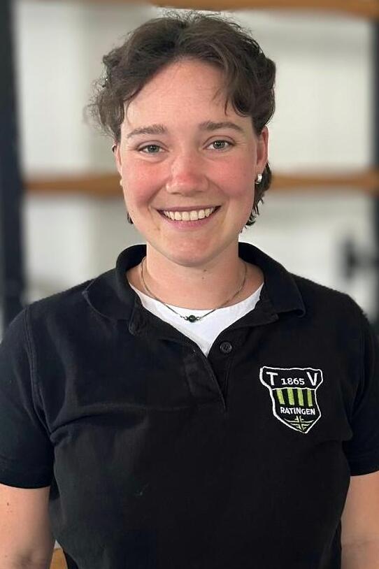 L&auml;chelnde Person mit kurzen Haaren, in schwarzer Polo-Uniform mit Logo, vor hellen Hintergrund.