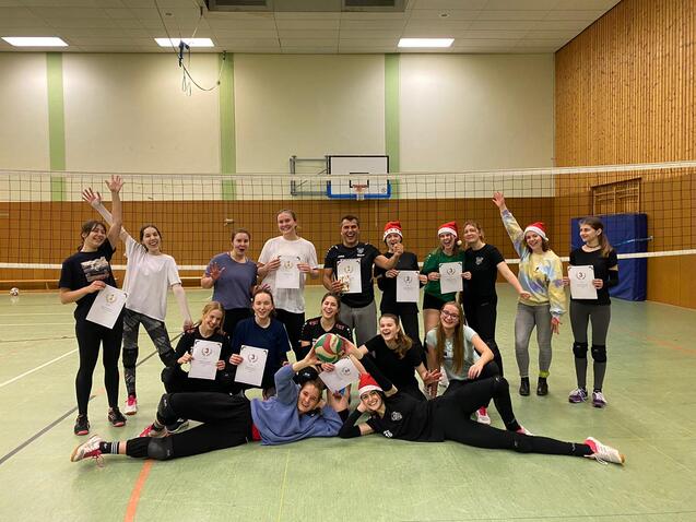 Gruppenshot von Volleyballspielerinnen mit Urkunden, im Hintergrund ein Volleyballnetz und Weihnachtsm&uuml;tzen.