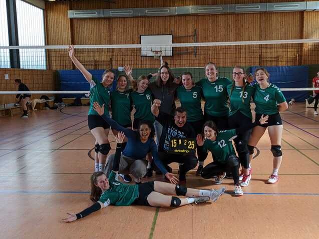 Gruppenshot eines Volleyballteams in gr&uuml;nen Trikots, posierend mit Punktetafel 15:0:25 in der Sporthalle.
