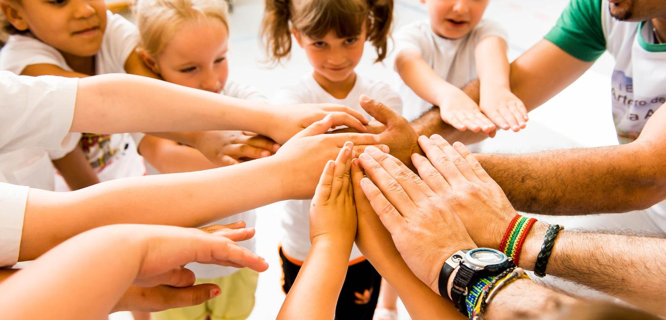 Kinder und Erwachsene legen ihre Hände in einem Kreis zusammen, symbolisieren Zusammenarbeit und Gemeinschaft.