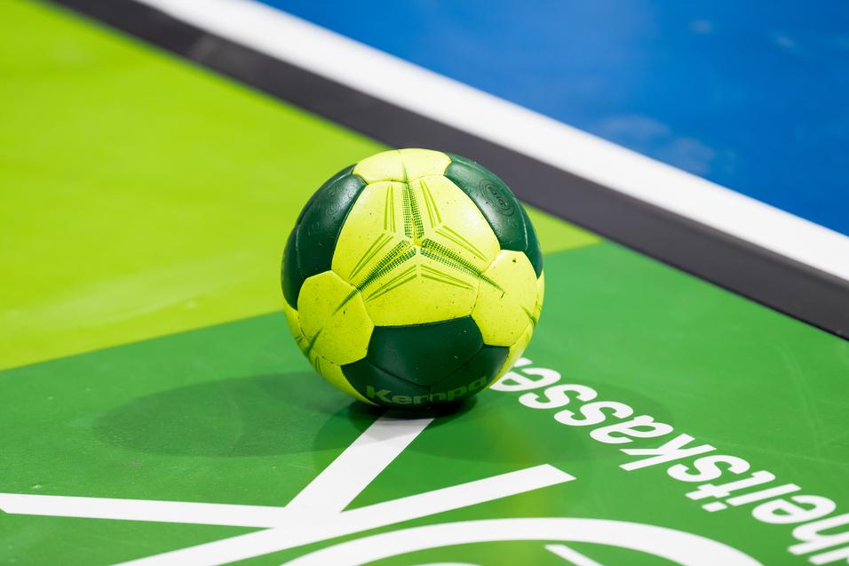 Grüner und gelber Handball liegt auf einer grünen Spielfläche mit weißem Schriftzug.